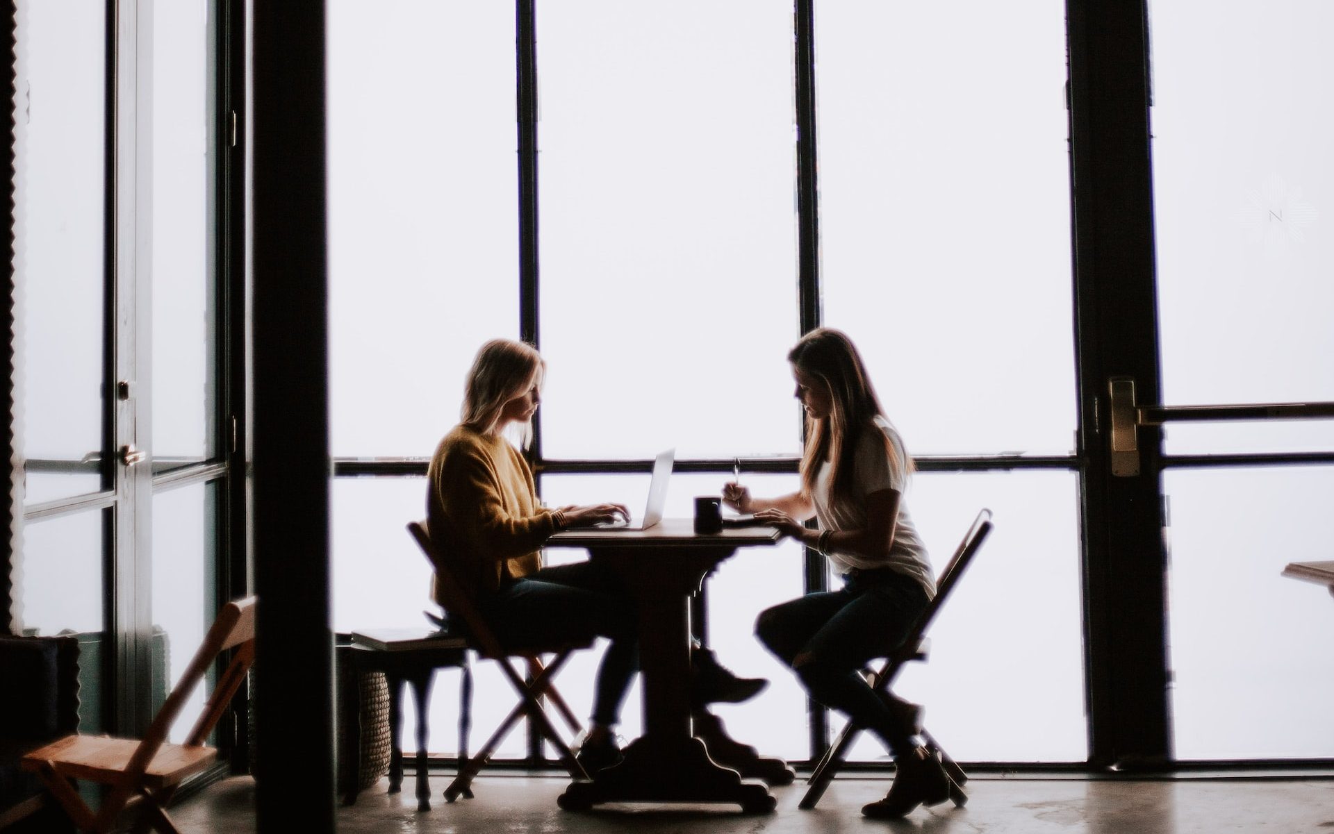 Silhouette of two people sitting in a coffee shop next to large windows