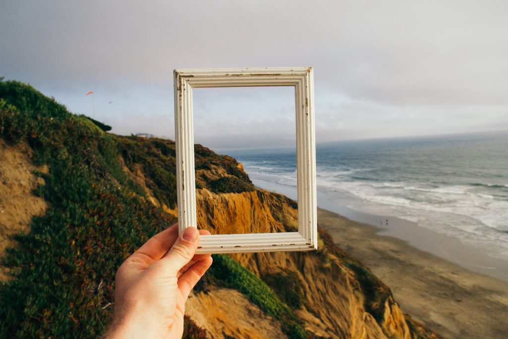 White picture frame held in front of a scenery of cliffs next to the sea