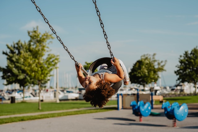 Girl with curly brown hair in a swing hanging upside down