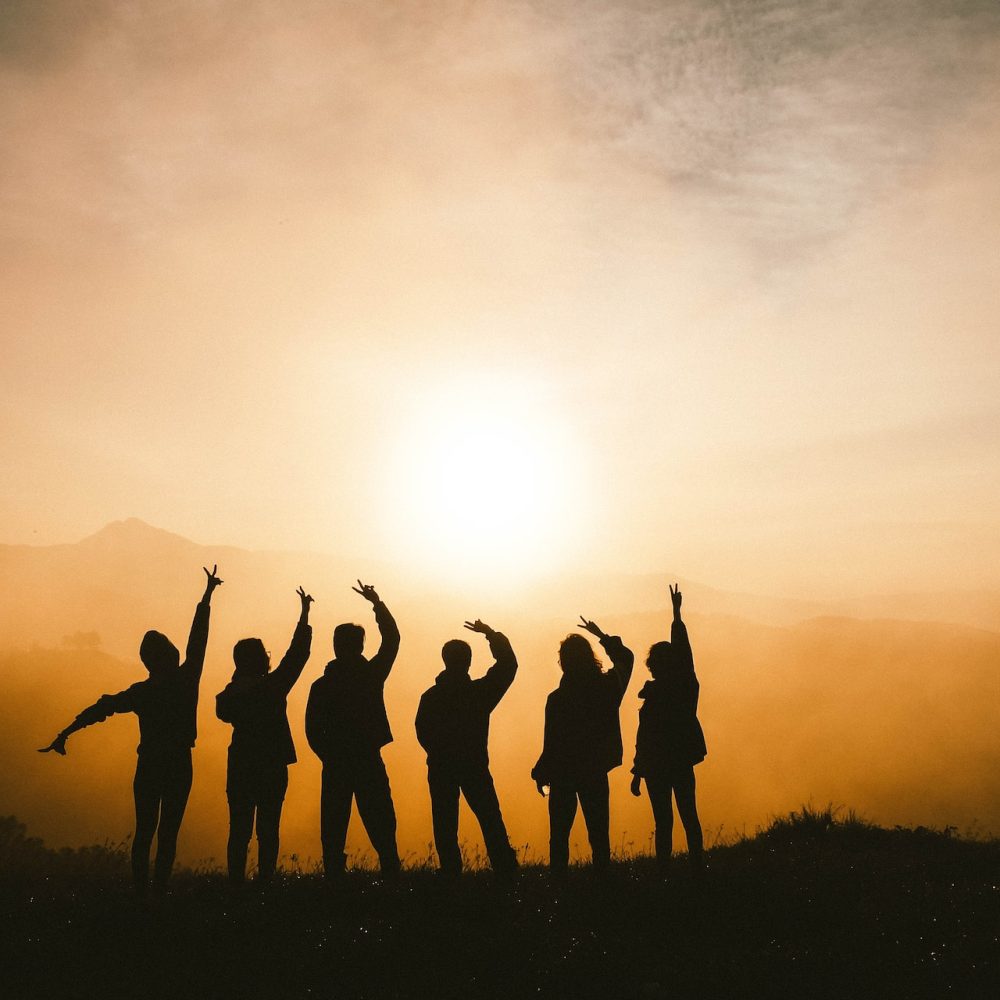 Silhouette of 6 people standing on a mountain with the sun in the horizon