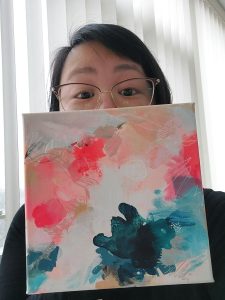 Crystal holding a piece of Miranda's abstract artwork in front of her face.